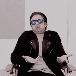 Video gif. A man with sunglasses leans back in a chair with his arms on the rests. He waves his hands around in a robotic fashion, and looks away with a large frown on his face, pretending he doesn't know anything. 