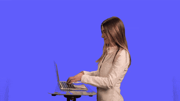 Video gif. A woman plunks on a laptop keyboard, then turns abruptly to smile at us.