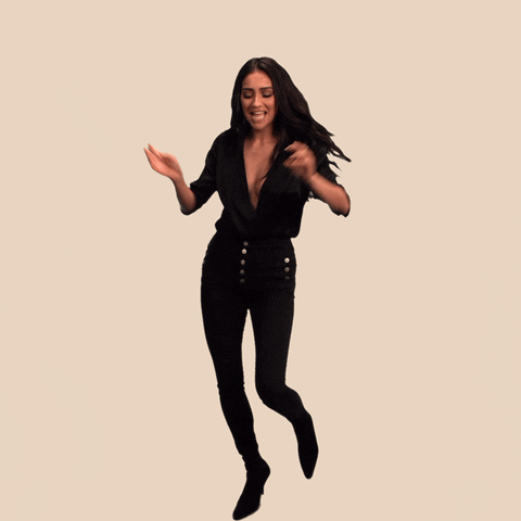 Video gif. Actress Shay Mitchell wearing all black, dances against a white background, arms in the air. She lifts one foot off the ground and shakes her booty for the camera.