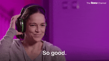 TV gif. Michelle Rodriguez on Player vs Player with Trevor Noah adjusts the headset on her head. She smiles and shakes her head out of amazement as she says, “So good.”