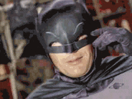 Movie gif. Adam West as Batman goofily bobs around while smiling.