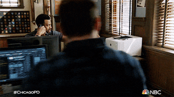 TV gif. Laroyce Hawkins as Kevin Atwater on Chicago PD is on the phone at his desk. He leans over to pull a paper out of the printer and stretches his arm out to hand the paper to the man who sits at the desk in front of him. 