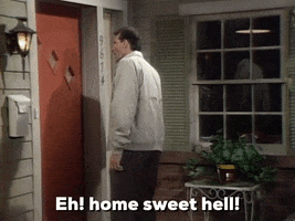 TV gif. Ed O'Neill as Al on Married with Children stands at the front door of a home and says, "eh! home sweet hell!" which appears as text.