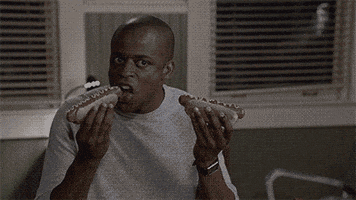 TV gif. Dulé Hill as Gus in Psych. He looks at us intensely as he double fists two hot dogs. He proceeds to take a bite of each one, never breaking eye contact with us as he does so.