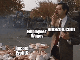TV gif. Mr. Bean stands happily in front of a table of desserts, stuffing his face with a cupcake and not noticing a giant military tank rolling by and completely destroying his car. Mr. Bean is labeled "Amazon dot com," the dessert table is labeled "record profits," the tank is labeled "inflation," and the car is labeled "employees' wages."
