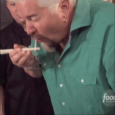 Celebrity gif. Guy Fieri shakes his head rapidly as he slurps up a noodle and looks at us with a hint of surprise.
