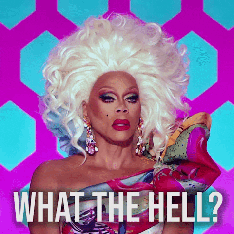 Reality TV gif. RuPaul in RuPaul's Drag Race wears a voluminous blonde wig and colorful one-shoulder top with a puffy sleeve. Text, "What the hell?"