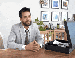 Celebrity gif. Comedian John Crist sits in a tuxedo at a desk with his fingers pressed together. He nods definitively before reaching into an open briefcase and pulling out papers. He says, "Let me in fact refer you to Exhibit B," which appears as text.