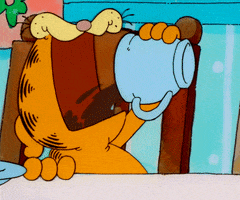 Cartoon gif. Garfield the cat sits at the dinner table with half lidded eyes. He grabs a cup, opens his mouth wide, and dumps all the coffee from the cup inside to wake himself up. 
