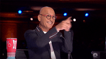 Reality TV gif. Howie Mandel as a judge on America's Got Talent. He points with both hands at the contestant, grinning at them in pride.