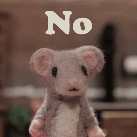 Video gif. Felt puppet mouse looks at us, shaking its head "no." It pauses to stare at us for a moment then its big black eyes blink closed just once against a blurred background. 
