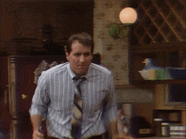 TV gif. Ed O'Neill as Al in Married... With Children sings and dances through the kitchen with a bottle in hand like he's having a little solo celebration.