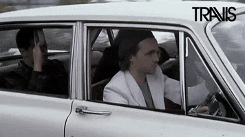 Music video gif. Fran Healy of Travis drives a vintage white car with cool focus as trees whiz by in the background. Text, "Is it Friday yet?