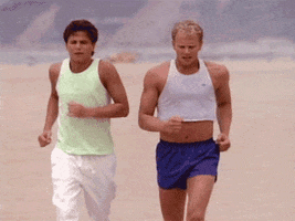 TV gif. David Lascher as Kyle on Beverly Hills 90210 jogs along the beach with Ian Ziering as Steve Sanders.