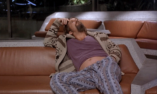 Movie gif. Jeff Bridges as The Dude from The Big Lebowski does not abide, alone and bored, rocking his leg back and forth. He leans back against a couch, scratching his head.