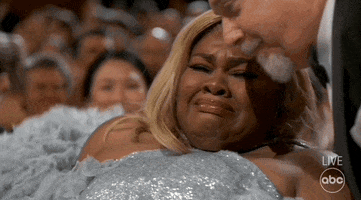 Oscars 2024 GIF. Da'Vine Joy Randolph holds back tears as she gets up from her seat to accept her award. She's overwhelmed by her win and Paul Giametti, who sits next to her, helps her up.