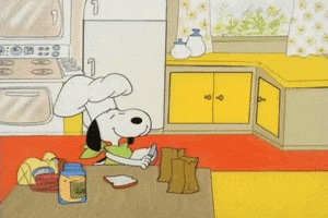 Peanuts gif. Wearing a chef's hat, a cheerful Snoopy spreads mayonnaise on a piece of bread. He tosses a slice of lunch meat over his head and catches it on the bread, topping it with another piece of bread. He repeats this process as Sally and Charlie Brown enter the scene. Snoopy bags the sandwiches and gives them to the children.