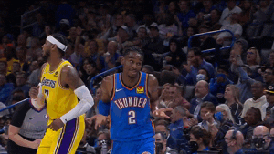 Sports gif. NBA Player Shai Gilgeous-Alexander of the Thunders runs in front of a Lakers player on the court. He tilts his head into his shoulder and shrugs as he’s running. 