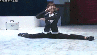 Video gif, Woman in a suit doing the front splits holds a flower between her teeth as she wiggles her feet, then holds out the flower as she scootches away.