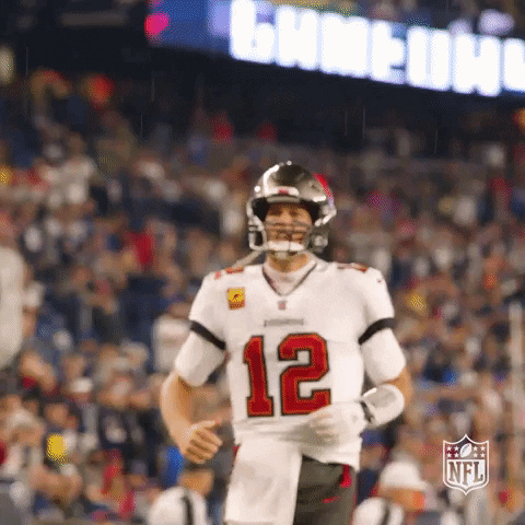Sports gif. NFL player Tom Brady, playing for the Buccaneers, pumps his fist like he’s throwing an invisible football, jogging and yelling in a haze of adrenaline from the game. 