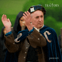 Sponsored gif. Traitors host Alan Cumming, dressed in a plaid hat and a velvet cloak, claps.