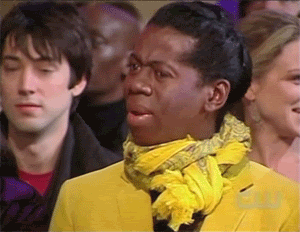 TV gif. Miss J Alexander from ANTM, in the audience of a fashion show, moves his hands around in a confused, "what the heck?" motion. He is wearing a loud yellow blazer with a matching yellow scarf. 