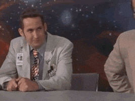 Movie gif. Harland Williams as Fred in RocketMan rests his arms on a desk, then looks up in shock and quakes with excitement before grabbing the person sitting beside him.