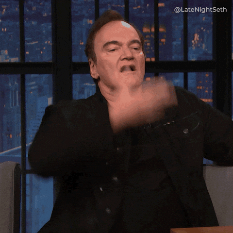 Late Night gif. Quentin Tarantino sits on the couch dramatically wipes the sweat from his forehead, acting relieved.