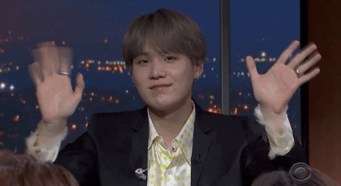 Late Night gif. Min Yoongi of BTS on The Late Show with Stephen Colbert looks at us with a smile as he waves both his hands very fast.