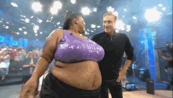 TV gif. A higher weight woman dances next to Maury Povich on Maury. She has her hand to her head and one arm around Maury as she dances and he smiles.