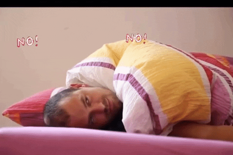 Video gif. Man lays on bed with his eyes open, he looks up as the word, “No” continuously floats around his head. He flails around in anger and pressed his face into the bed.