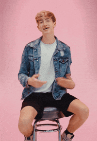 Video gif. Cash Baker, an influencer, is sitting on a stool explaining something and gesturing with his hands.