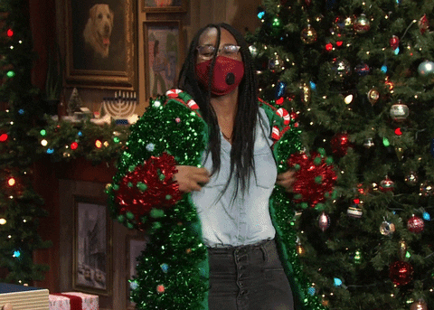 Tonight Show gif. A woman standing in front of a Christmas tree, in a den fully decked out in Christmas decor, turns to the left, then to the right, showing off her fully decked out Christmas sweater, complete with garland and ornaments that make her look like a Christmas tree.