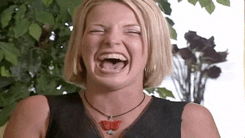 Video gif. Woman laughs hysterically, scrunching her nose, and moving around in her seat.