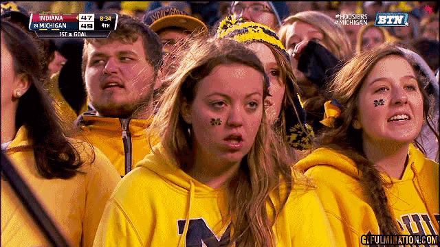 Sports gif. University of Michigan football fan stares ahead with her mouth open, dumbfounded.