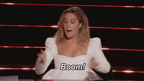 Reality TV gif. In a clip from The Masked Dancer, Ashley Tisdale wears a white dress as she holds up her pointer fingers and exclaims: Text, "Boom!"