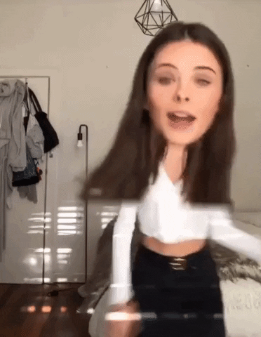 Celebrity gif. Using a filter that makes her head look three times too big, model Meika Woollard dances awkwardly in her bedroom.