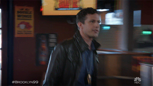 TV gif. Andy Samberg as Jake Peralta on Brooklyn Nine-Nine goes up to a bar and without even looking at him, high fives Joe Lo Truglio as Charles Boyle. Charles does a small spin as he high fives Jake.