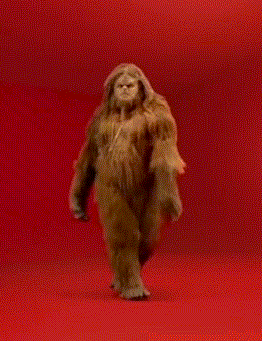 Video gif. The ape like Sasquatch struts as he wears a chain around his neck and walks seductively towards us. 