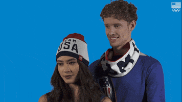 Sports gif. Evan Bates stands behind Madison Chock, and Chock rolls her eyes and sticks out her tongue, as if she is disgusted.