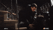 TV gif. Octavio Pisano as Joe on Law & Order : Special Victims Unit, leans over an unconscious woman, picking her up from her face down position at the foot of a staircase. 