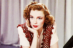 Celebrity gif. Judy Garland looks poised with her curled hair and red lipstick but anxiously taps her polished fingers against her cheek, letting out a small, nervous sigh.