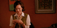 TV gif. Elisabeth Moss as Peggy from Mad Men smiles as she counts a pile of bills clutched in her hands. 