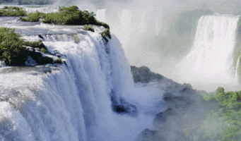 Video gif. A sweeping view of waterfalls cascade water down steep drops, lush greenery peeking through at the top and bottom.
