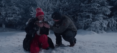 Music video gif. Ed Sheeran in the Merry Christmas music video is kneeling next to a girl who holds a cat in her arms. It snows all around them and eventually the girl lets the cat go.