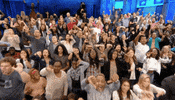 Reality TV gif. The audience at The Maury Show are all standing up and are booing the stage.