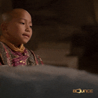 Video gif. A child dressed like a monk looks up with a smile and gives a big thumbs up. 
