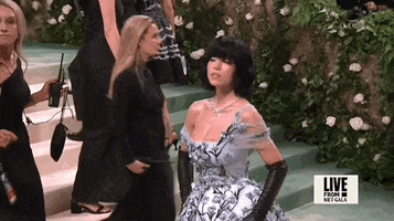 Met Gala 2024 gif. Sydney Sweeney wearing a silvery Miu Miu gown and bold jet-black bobbed wig, drops her chin in slomo, sultry and aloof.