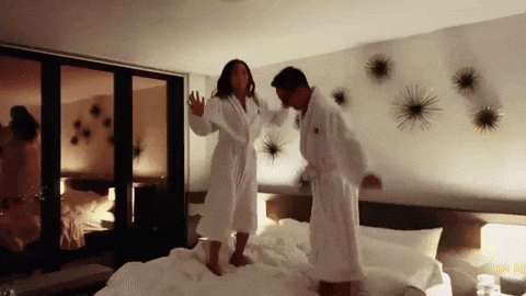 como reservar um quarto em espanhol 

DESCRIÇÃO DA IMAGEM: Duas pessoas estão usando roupões felpudos e pulando em cima de uma cama de hotel. 