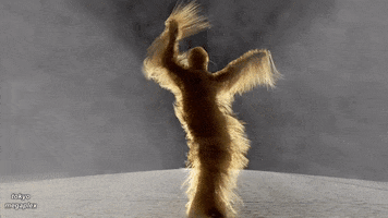 Video gif. A light shines behind a figure with long blond hair on every inch of their body dances the samba, the long hair flowing dramatically with each movement.